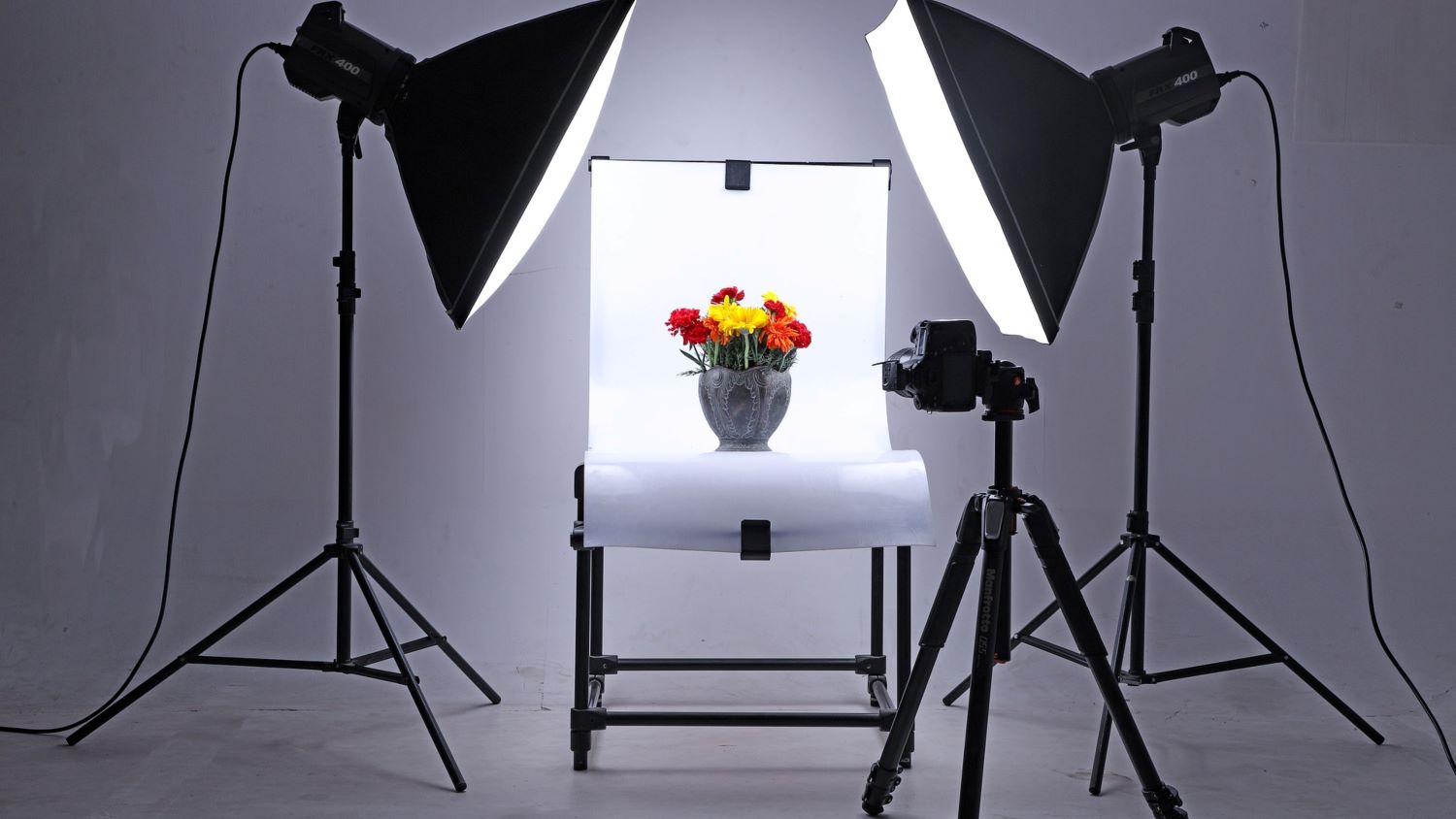 A professional product photography studio setup with two lights, a camera on a tripod, and a white backdrop, ready to capture a product for brand visualization.